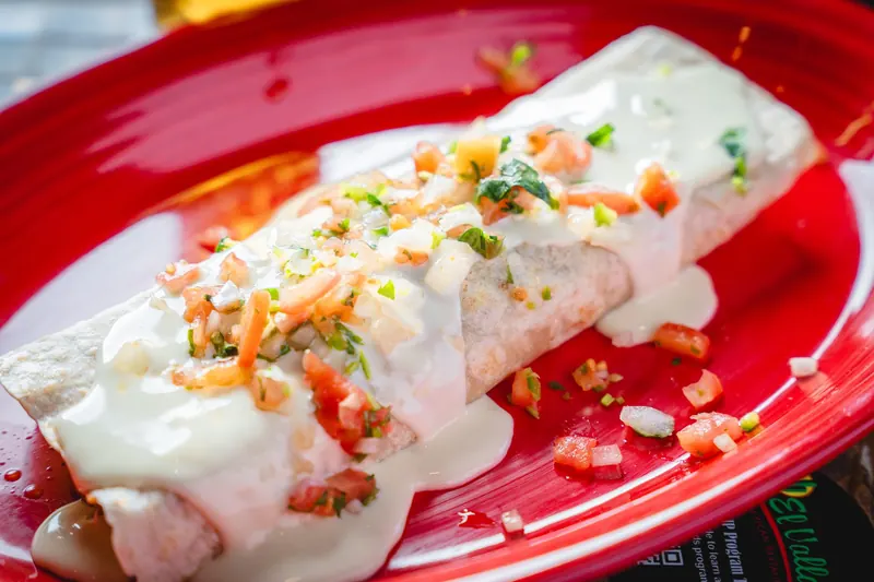 Pancho Burrito under white queso on a red platter