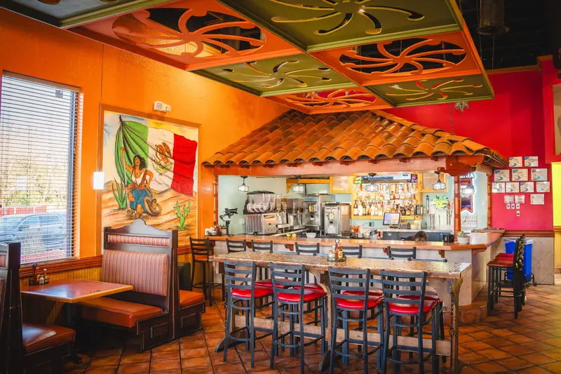 Monroe bar with red stools under a tile roof and a mural of a woman with a Mexican flag